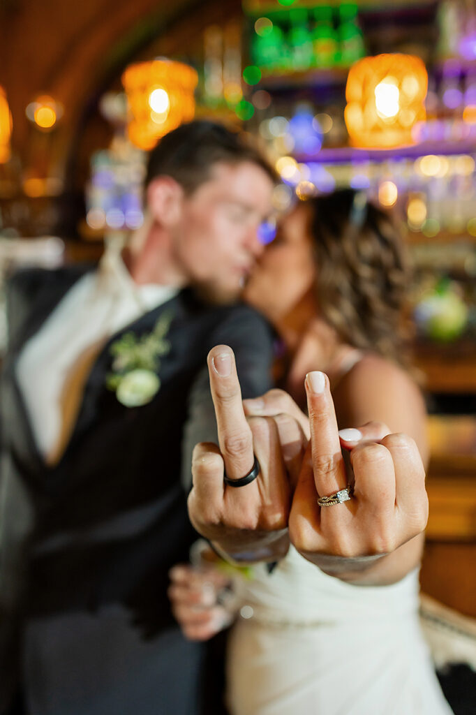 married couple elopement newlyweds at the bar holding up ring fingers and kissing in Bonez downtown colorful Crested Butte restaurant