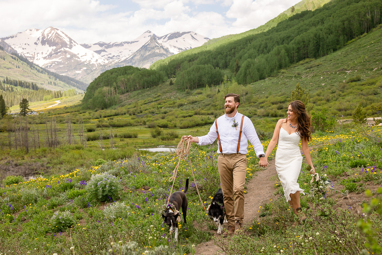 couple holding hands with dogs on leash walking scenic mountain view background newlyweds small wedding Crested Butte photographer Gunnison photographers Colorado photography - proposal engagement elopement wedding venue - photo by Mountain Magic Media