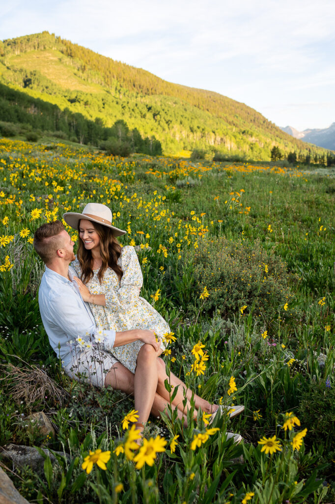 engagements woman in hat sitting on man's lap in wildflowers wildflower festival Crested Butte photographer Gunnison photographers Colorado photography - proposal engagement elopement wedding venue - photo by Mountain Magic Media