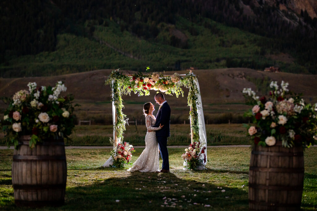 Couple at sunset under floral arch at Crested Butte Town Ranch wedding venue.