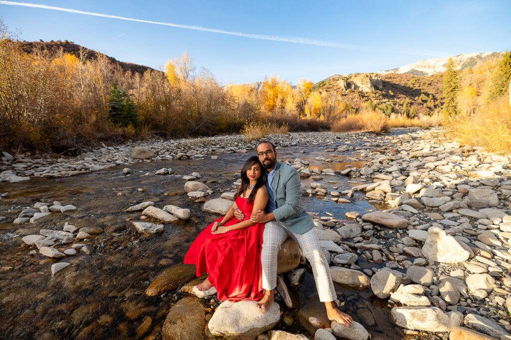 engaged couple sitting on rock wearing red dress and barefoot