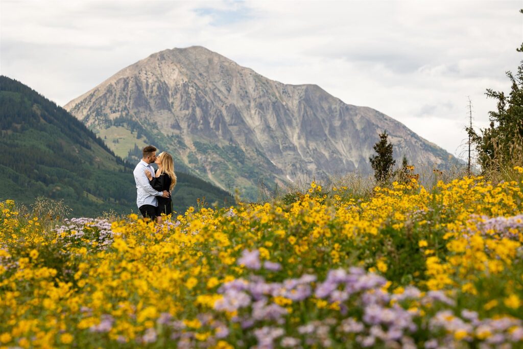 A couple kiss in a field of wildflowers in the mountains Colorado Proposal Photographer