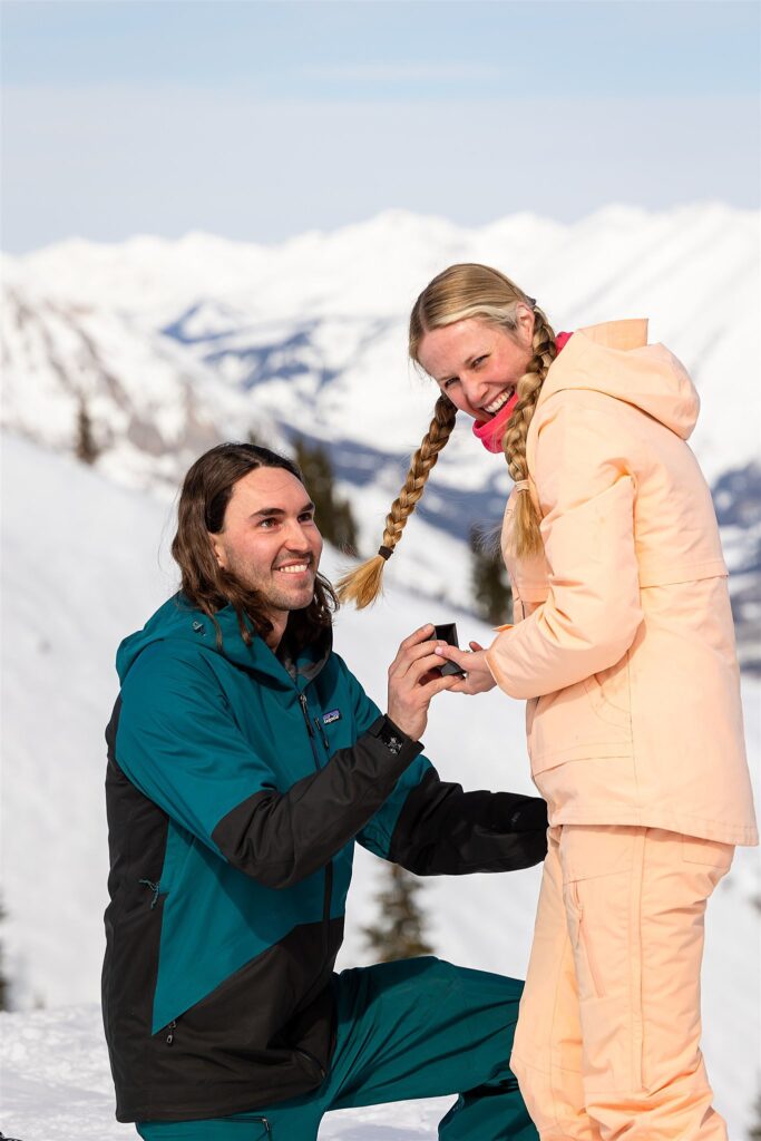 A man in a ski suit proposes to his girlfriend on a mountain top Colorado Proposal Photographer