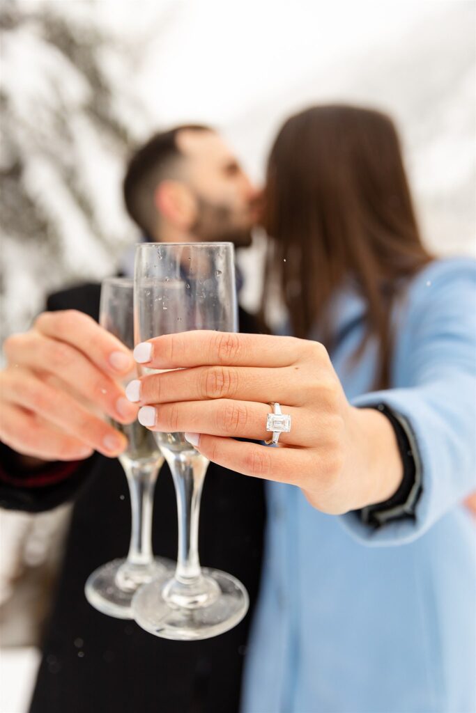A couple hold out champagne glasses while kissing in the snow