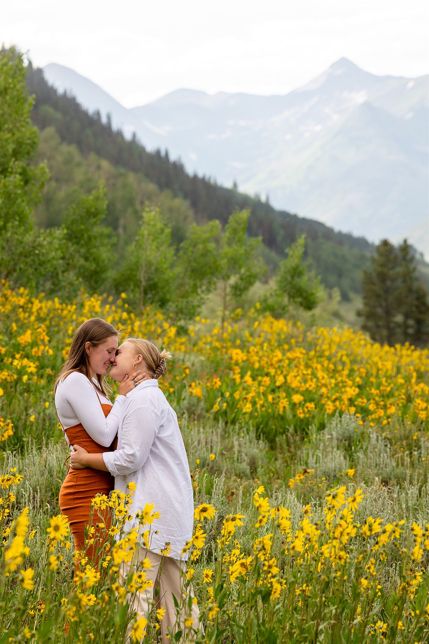 A couple kisses while standing in a field of wildflowers on a mountainside