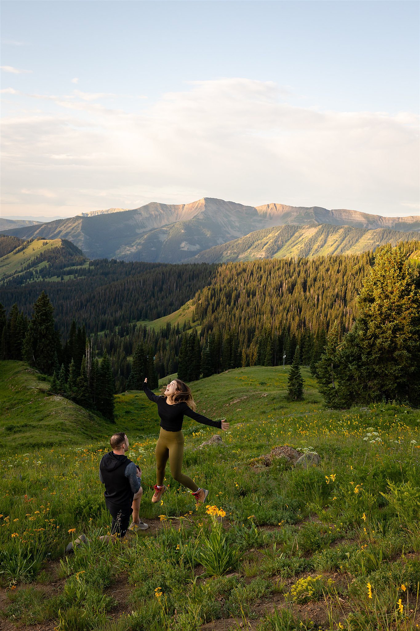 A woman jump for joy in a mountain field while being proposed to Colorado Proposal Photographer