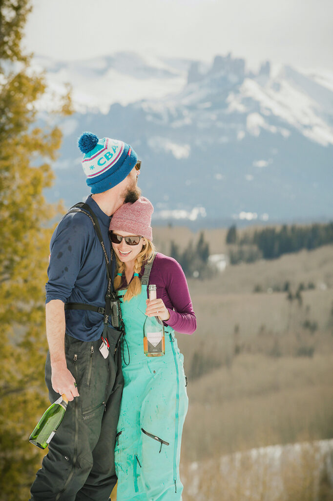 newly engaged couple holding champagne bottles in the backcountry of Crested Butte, celebrating their surprise proposal