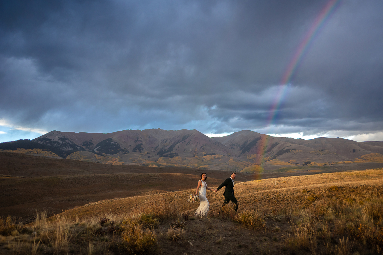 A couple holds hands and walks under a rainbow in Crested Butte on their wedding day