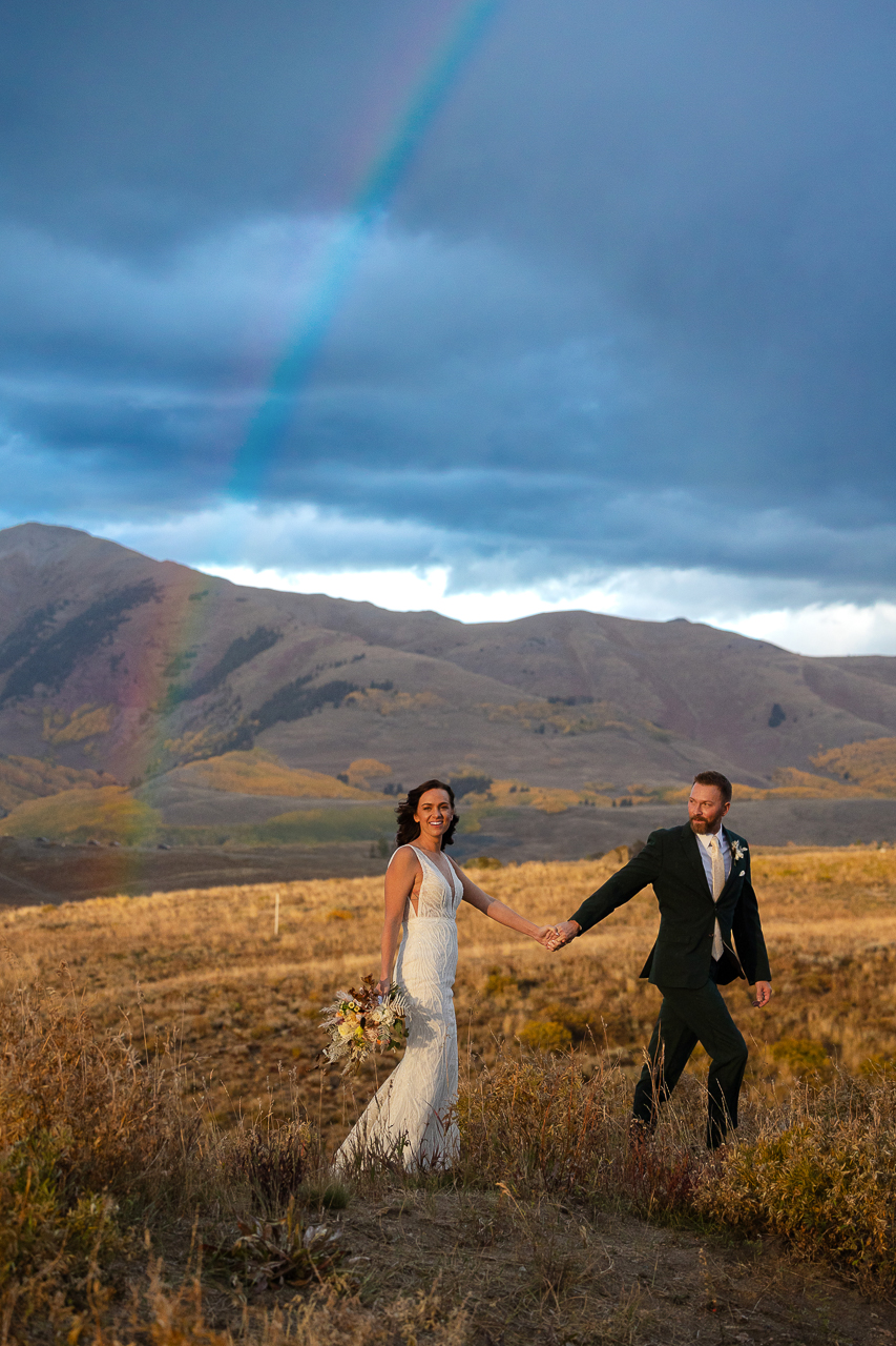 A couple holds hands and walks under a rainbow in Crested Butte on their wedding day