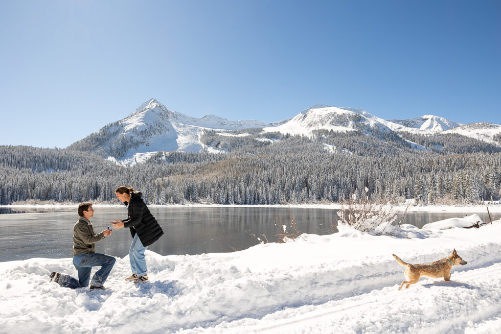 Surprise Proposal at winter lake near Crested Butte. Surprised woman holding man's hands with engagement ring.