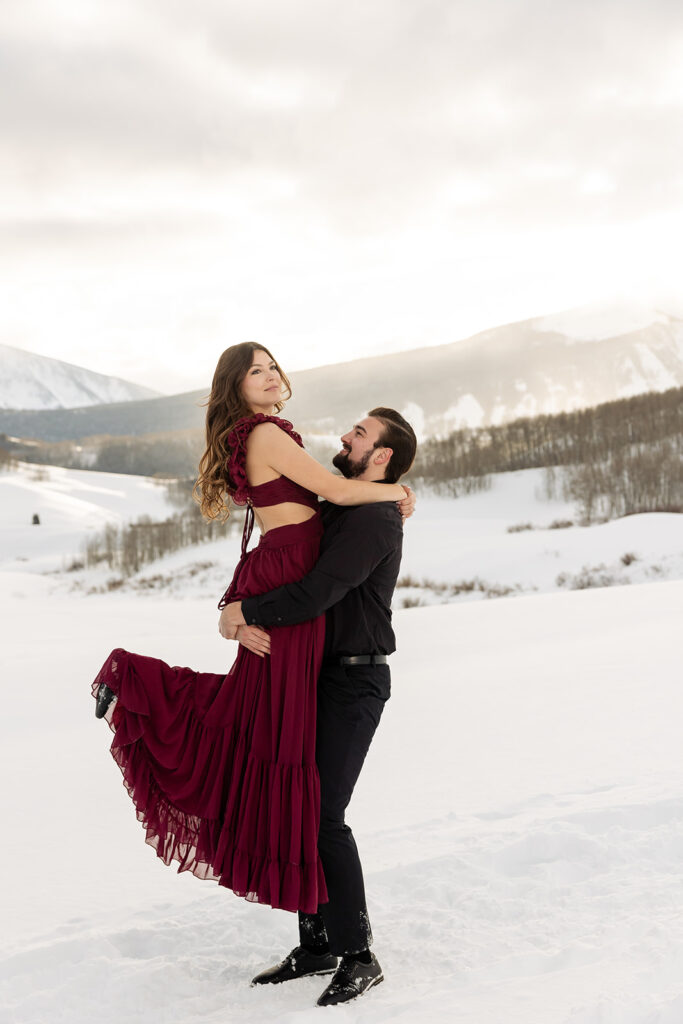 Crested Butte proposal pricing client review. Engagement couple with woman wearing a red dress and man wearing black lifting her. for Proposal Packages