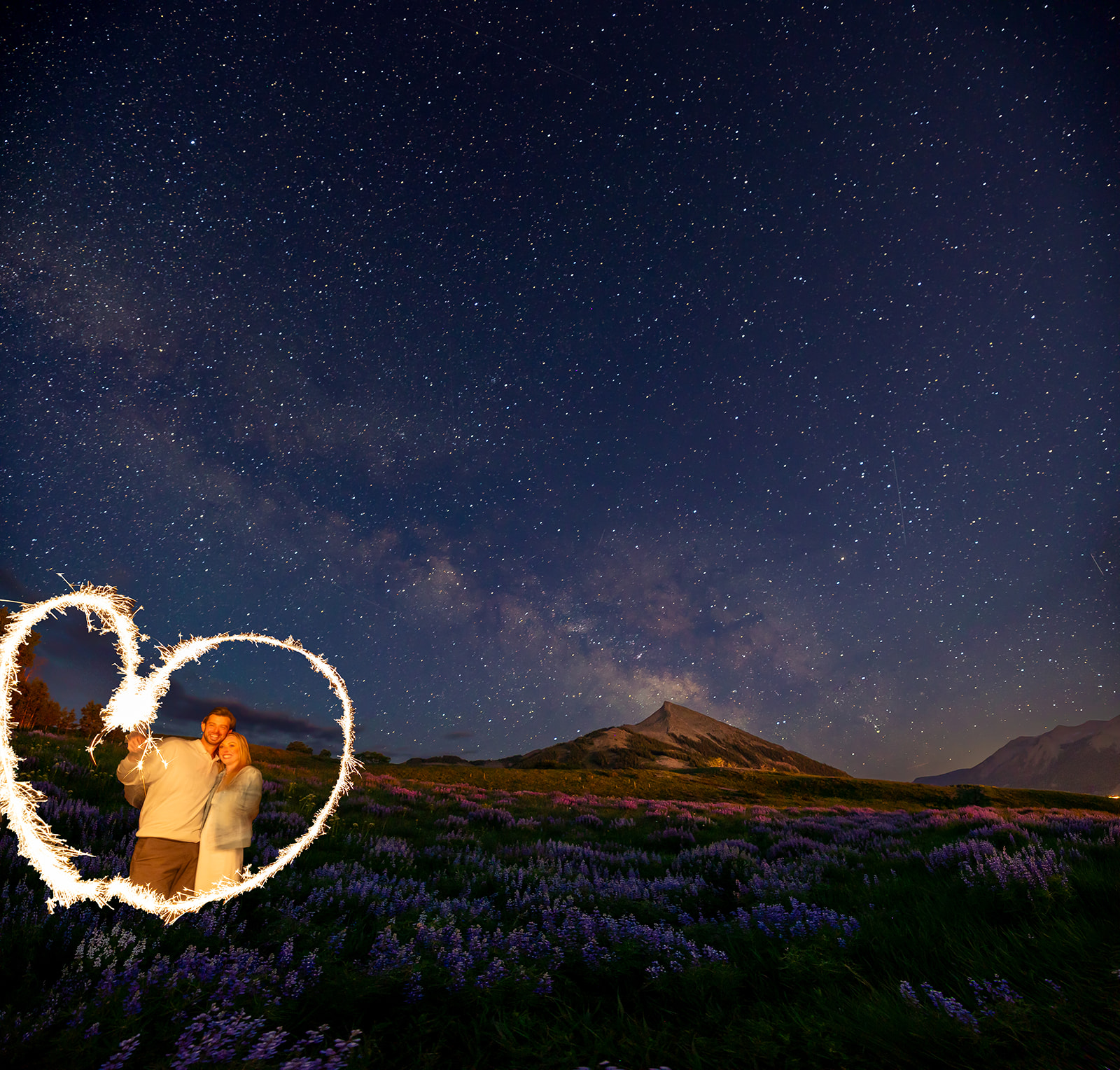 Crested Butte engagement photographer documents starry sky astrophotography with sparklers making a heart shape around engaged couple