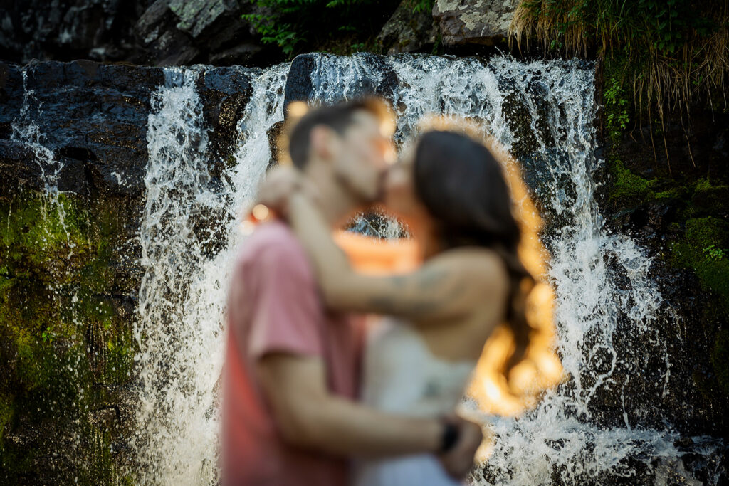 Artistic engagement photo with a couple softly blurred kissing in front of a sharp cascading waterfall near Crested Butte