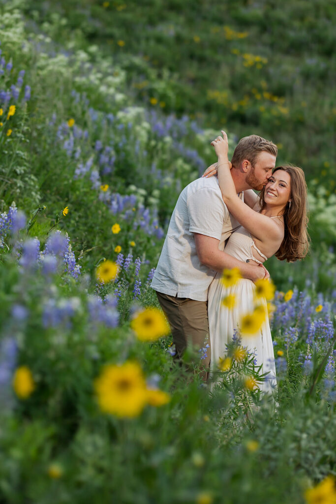 Engaged couple walking through purple lupine wildflower field with sweeping Crested Butte mountain valley in background at sunset