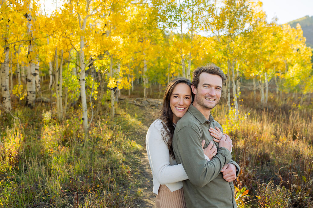 Engaged couple embracing on the Woods Walk trail with golden aspen trees behind them near Crested Butte Colorado during a fall engagement session